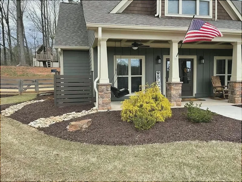 Fresh dark mulch beds with river-rock edging in front of a house