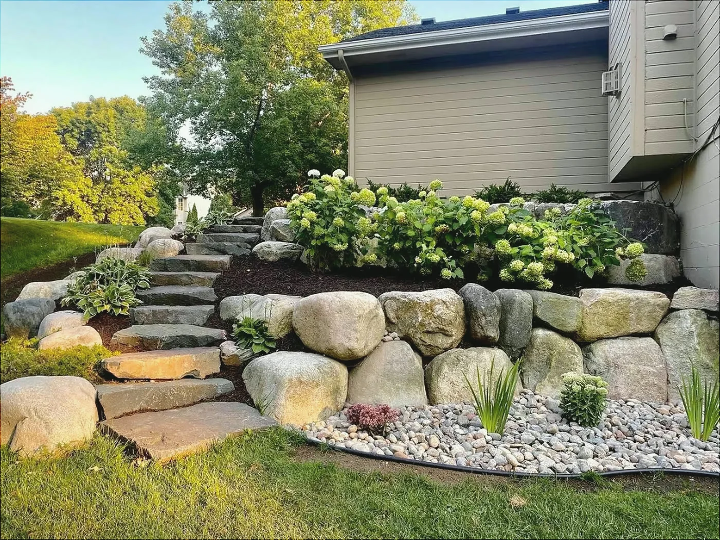 Boulder retaining wall with natural stone steps and hydrangeas